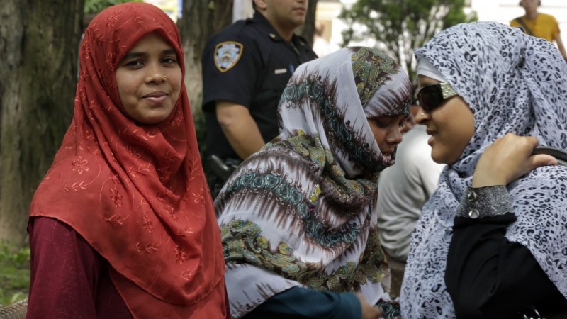 Three Muslim women in hijabs gather under the watchful eyes of NYPD at a rally.