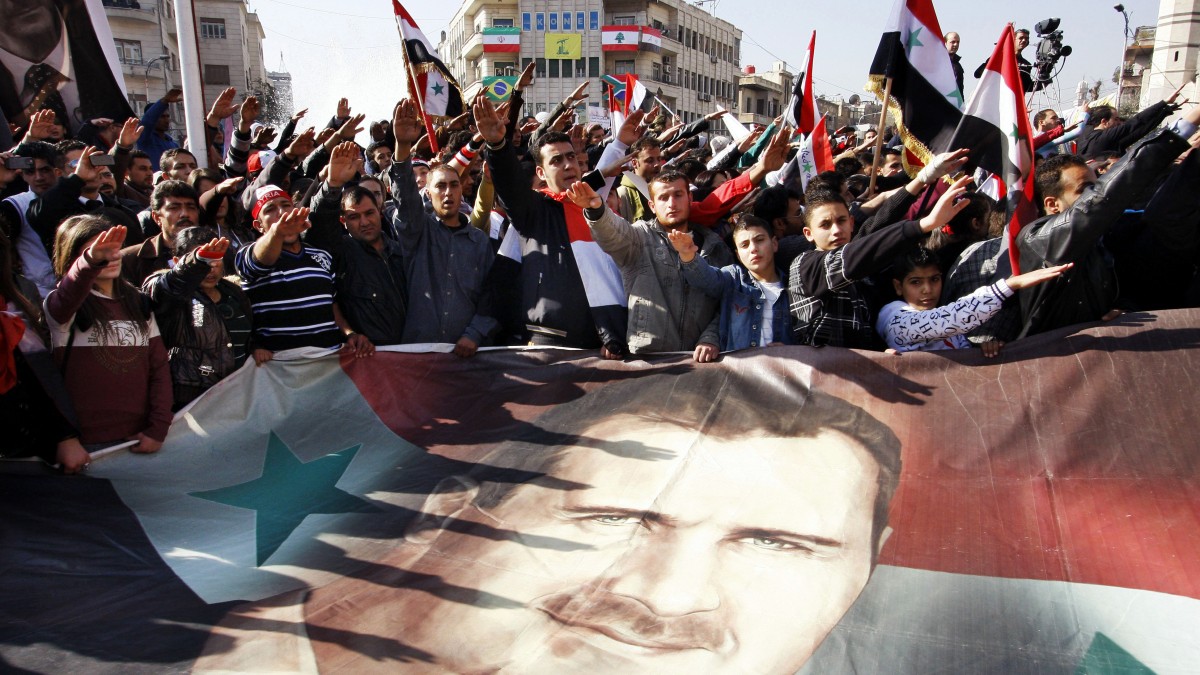 FILE - In this Monday, Dec. 19, 2011 file photo, Syrians hold a large poster depicting Syria's President Bashar Assad during a rally in Damascus, Syria. Some activists expressed regret that one year later their "revolution" against President Bashar Assad's rule had become mired in violence. (AP Photo/Muzaffar Salman, File)