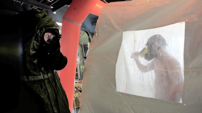 A crew member of the Danish warship Esbern Snare enters a decontamination shower wearing a gas mask, while another crew member waits, during drills at sea between Cyprus and Syria, Sunday, Jan. 5, 2014. Two cargo ships and their warship escorts set sail at waters near Syria where they will wait for orders on when they can head to the Syrian port of Latakia to pick up more than 1,000 tons of chemical agents. (AP Photo/Petros Karadjias)