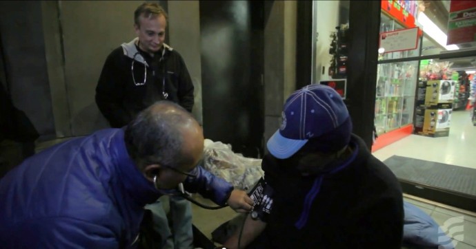 Dr. Jim Withers watches over as a medical student gives aid to a homeless person.