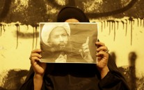 A Bahraini anti-government protester holds up a picture of jailed Saudi Sheik Nimr al-Nimr during clashes between police and protesters in Sanabis, Bahrain, a suburb of the capital Manama, Wednesday night, Oct. 15, 2014. The well-known Shiite cleric was executed January 2, 2016 in Saudi Arabia, sparking fears of renewed unrest from his supporters in the kingdom and neighboring Bahrain. Anti-government graffiti on the wall behind her reads, "We are steadfast and committed to our oath."