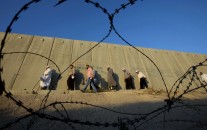 Palestinian men walk past a section of Israel's apartheid wall to cross the Qalandia checkpoint on their way to pray at the Al-Aqsa Mosque in Jerusalem, on the fourth Friday of the Muslim holy month of Ramadan, at the Qalandia checkpoint between the West Bank city of Ramallah and Jerusalem, Friday, July 10, 2015.