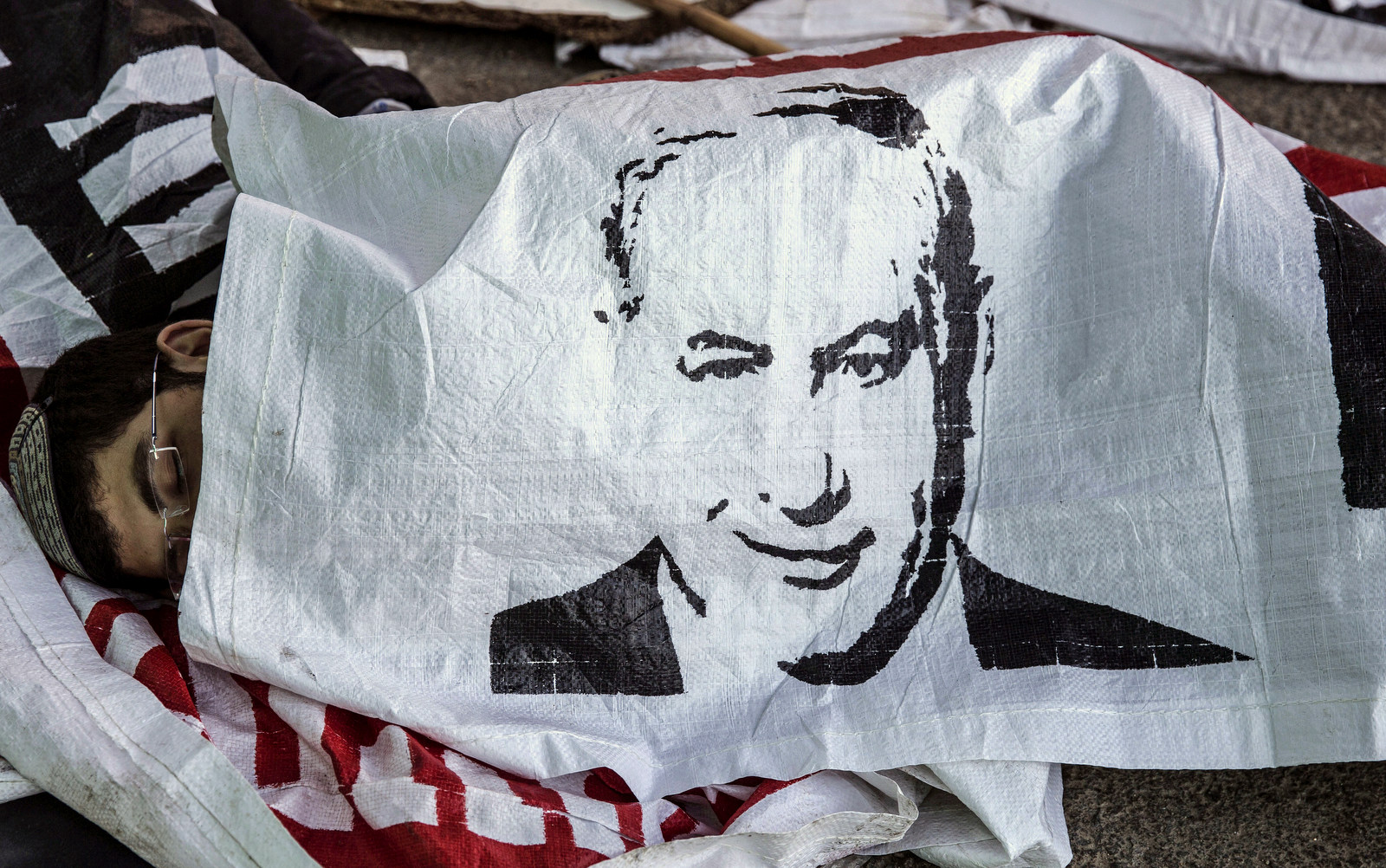 An Israeli settler sleeps under a banner of Israeli Prime Minister Benjamin Netanyahu, in the Jewish settlement of Beit El after a night stand off with police, near the West Bank town of Ramallah, Wednesday, July 29, 2015. The Israeli Prime Minister's office said Wednesday it has approved the "immediate construction" of 300 housing units in the West Bank settlement of Beit El. The announcement came amid a standoff, where Israeli settlers clashed with Israeli forces as authorities began to dismantle the contested West Bank settlement housing complex after Israel's Supreme Court ruled Wednesday that it must be demolished. (AP Photo/Tsafrir Abayov)