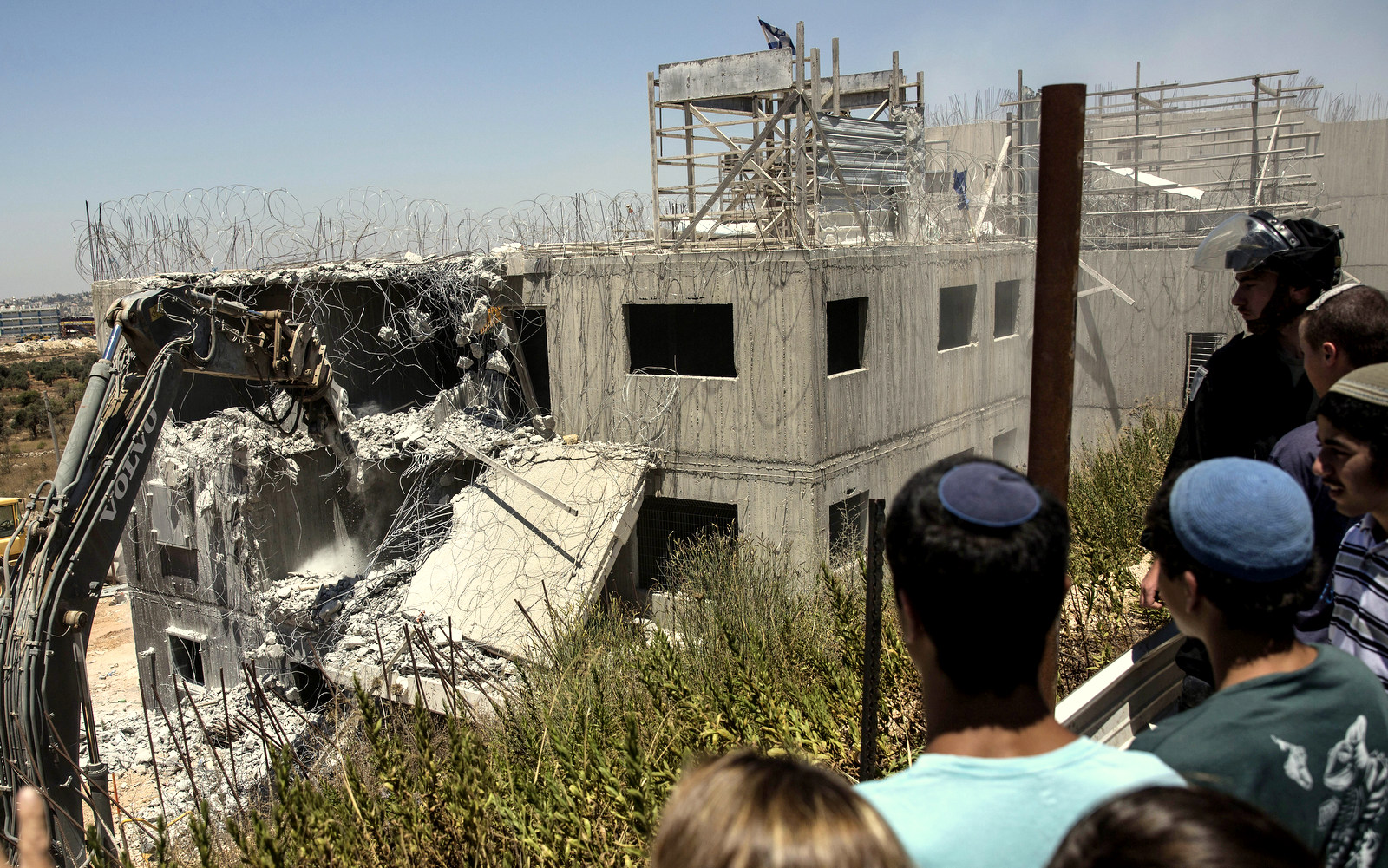 Young Israeli settlers watch the demolition of a building at the Jewish settlement of Beit El, near the West Bank town of Ramallah, Wednesday, July 29, 2015. Israeli bulldozers began demolishing a contested housing complex in a West Bank settlement on Wednesday as the prime minister’s office announced the “immediate construction” of some 300 new units at another location in the same settlement and advanced plans for about 500 new units in east Jerusalem.  (AP Photo/Tsafrir Abayov)