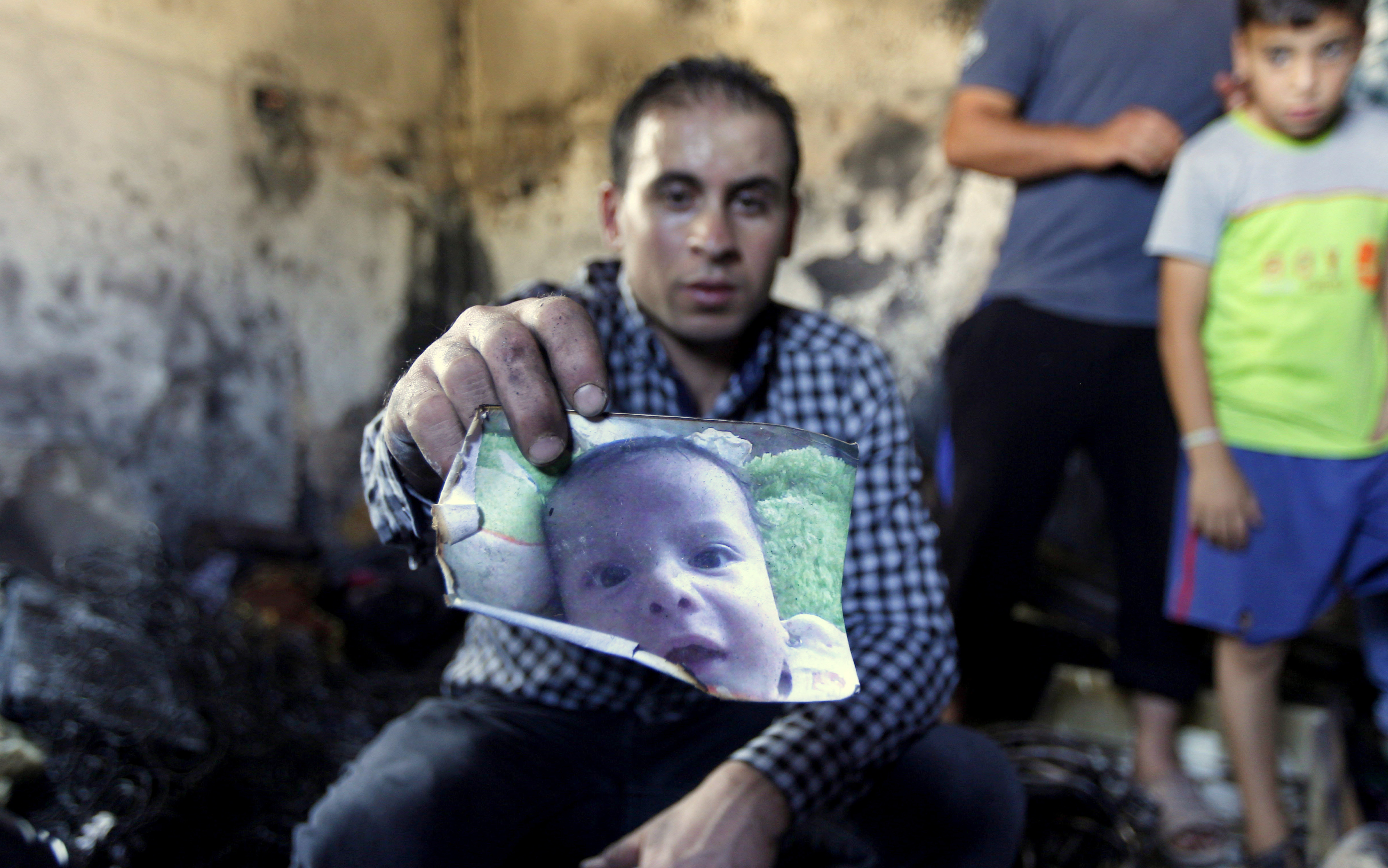 A relative holds up a photo of a one-and-a-half year old boy, Ali Dawabsheh, killed in a house that had been torched in an attack by Jewish extremists in Duma village near the West Bank city of Nablus, Friday, July 31, 2015. (AP Photo/Majdi Mohammed)