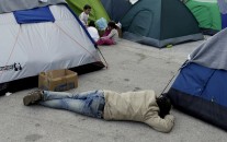 A man sleeps on the ground as children play outside their tents at the Athens' port of Piraeus, where over 5,500 refugees and migrants stay, on Monday, March 21, 2016. Greek Prime Minister Alexis Tsipras says an international agreement to limit the number of refugees and migrants traveling to Europe cannot be properly implemented unless smugglers on the Turkish coast are stopped. (AP Photo/Thanassis Stavrakis)
