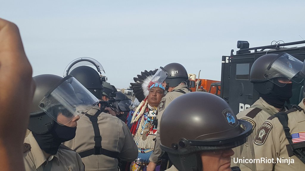 Police arrest an elder in ceremonial garb who was praying near Cannon Ball, N.D. (Photo: Unicorn Riot/Creative Commons)