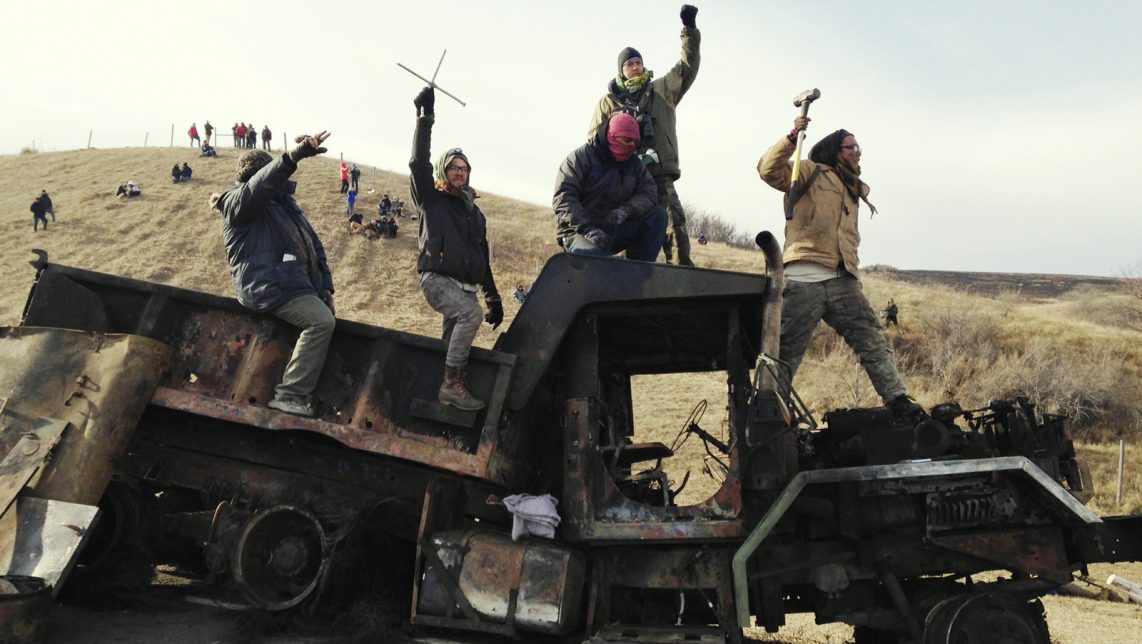 Protesters against the Dakota Access oil pipeline stand on a burned-out truck near Cannon Ball, N.D., Monday, Nov. 21, 2016, that they removed from a long-closed bridge on Sunday on a state highway near their camp in southern North Dakota. Opponents skirmished with law officers late Sunday and early Monday. (AP Photo/James MacPherson)