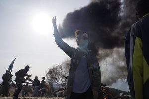 Gabriella Scarlett, a water protector from Canada, signals for peace as a fire barricade burns off County Road 134. Behind her, water protectors establish a fire barricade to hold police back from the site of construction of the Dakota Access pipeline. Oct. 27, 2016  (Derrick Broze for MintPress)