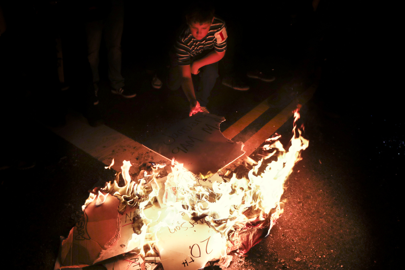 A young protestor feeds a fire of protest signs during a demonstration outside the National Press Building ahead of the presidential inauguration, Thursday, Jan. 19, 2017, in Washington. (AP/John Minchillo)