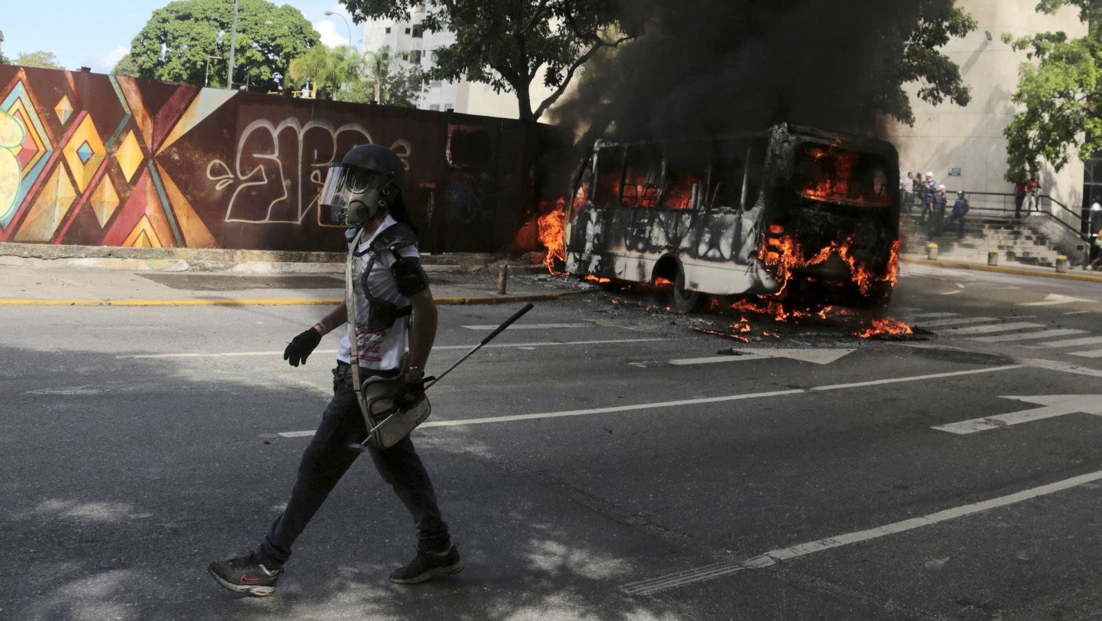 A protester wearing a gas mask and carrying a golf club walks to join fellow protesters, past a burning public transportation bus in Caracas, Venezuela, May 13, 2017. The anti-government protest movement that has drawn masses of people into the streets nearly every day since March, continued on Saturday. (AP/Fernando Llano)