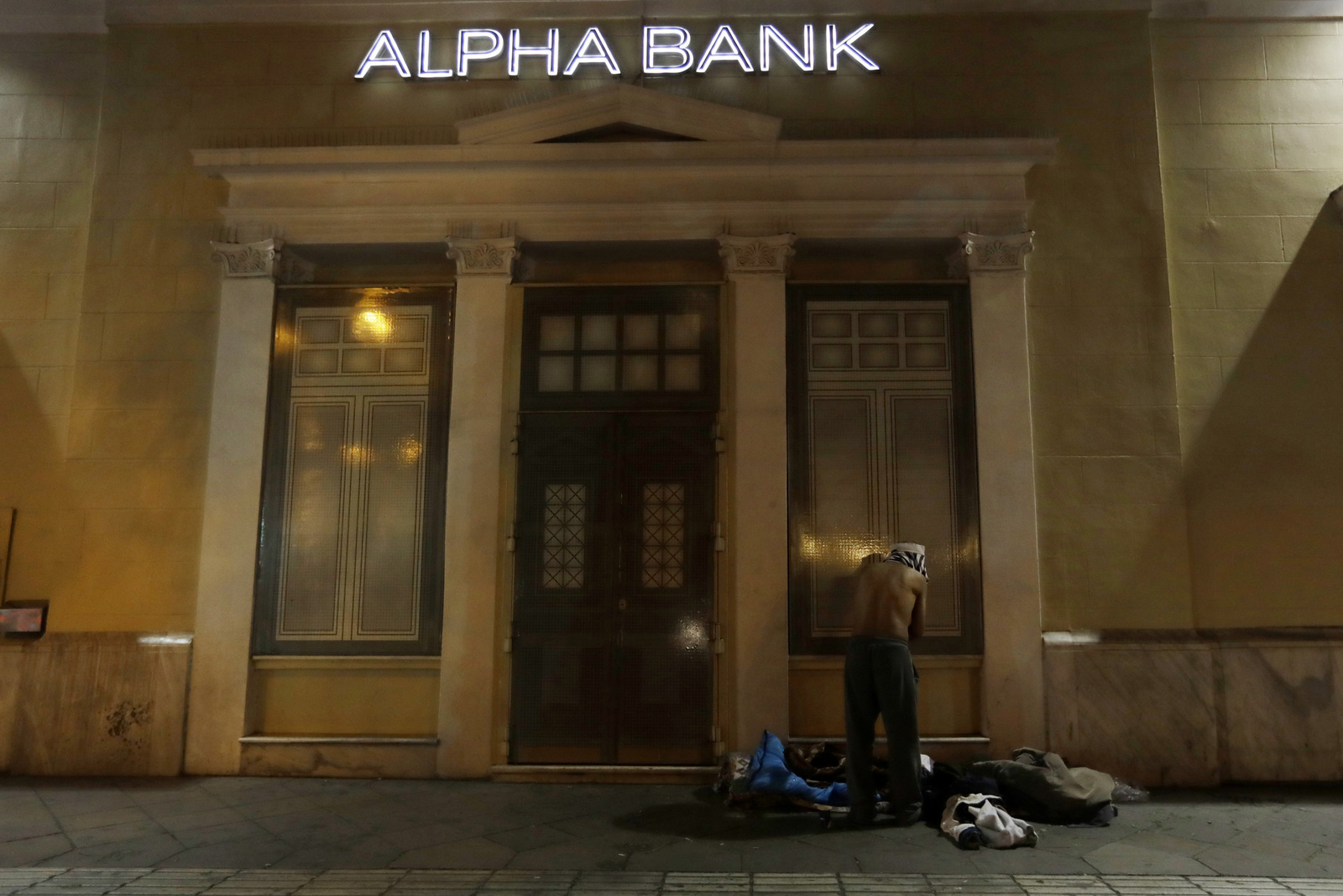 A homeless person changes clothes outside a bank in central Athens. Nearly one-in-four Greeks are unemployed and receive no benefits. Poverty rates have surged here since the start of the crisis in late 2009, with nearly 36 percent of the country living in financial distress. (AP/Thanassis Stavrakis)