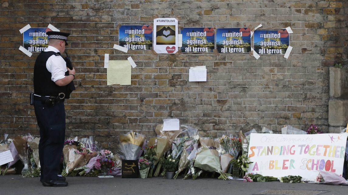 A police officer stands near floral tributes in Finsbury Park after an incident where a van struck pedestrians, in London.