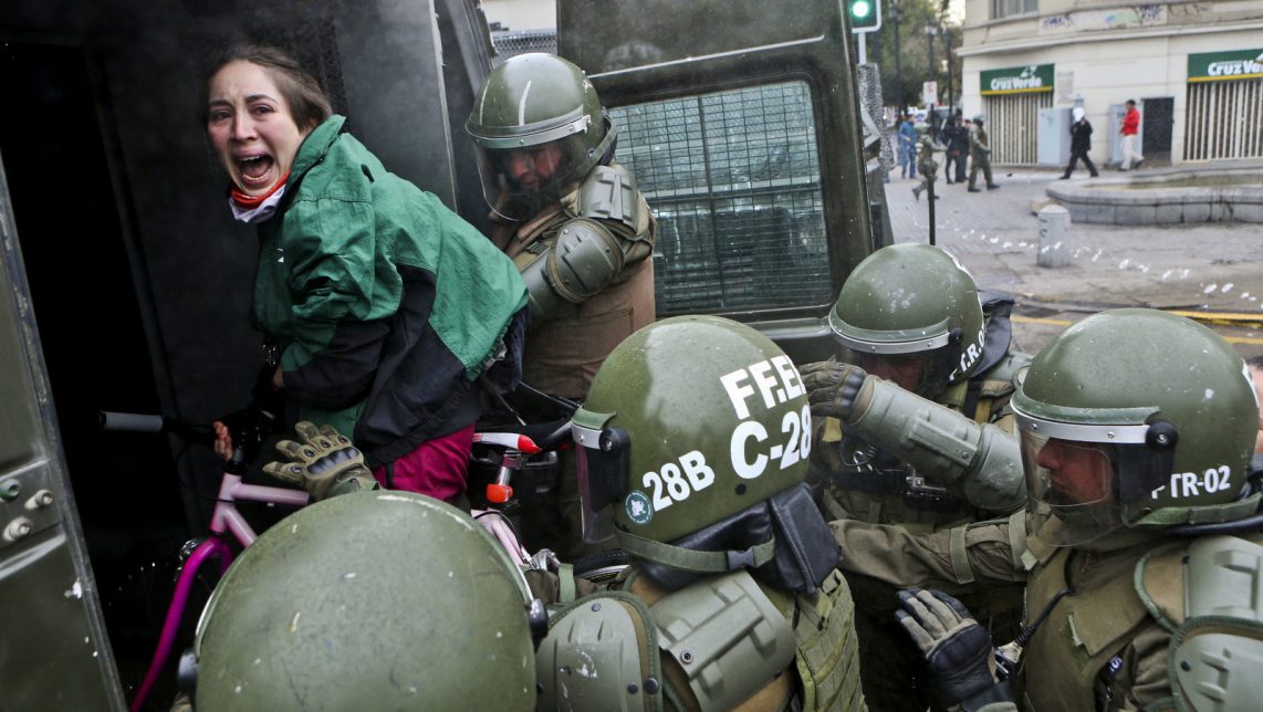 A woman, while on her bicycle, is lifted and placed by police into a paddy wagon during a protest march demanding the government overhaul the education funding system that would include canceling their student loan debt, in Santiago, Chile. (AP/Esteban Felix)