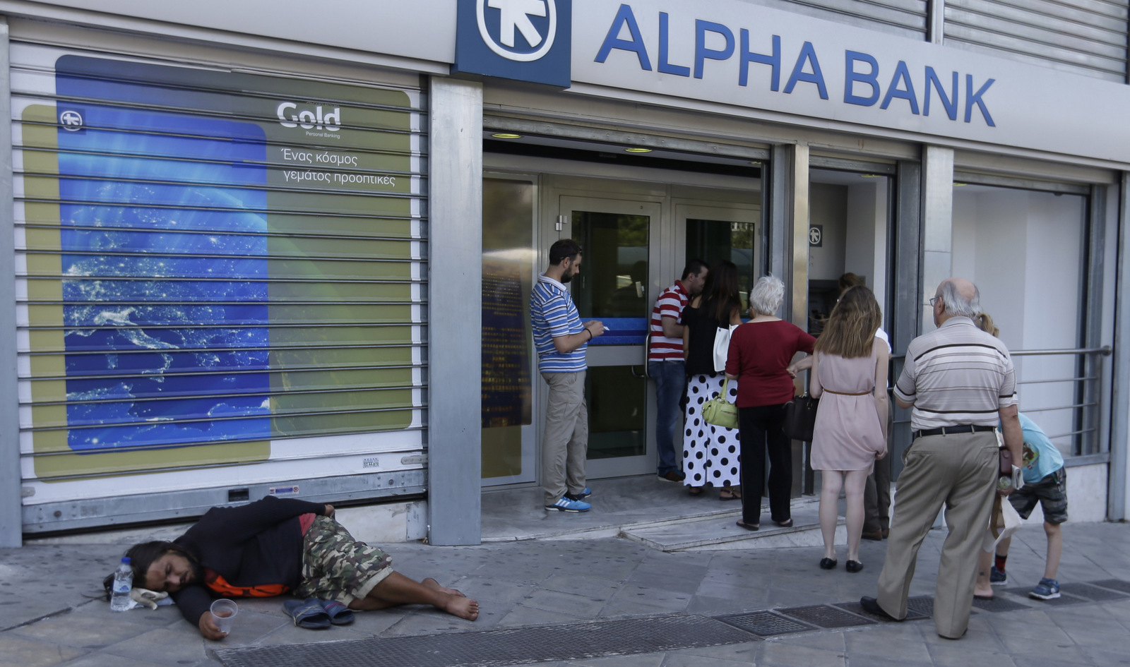 People queue in front of a bank for an ATM as a man lies on the ground begging for change, in Athens. (AP/Thanassis Stavrakis)