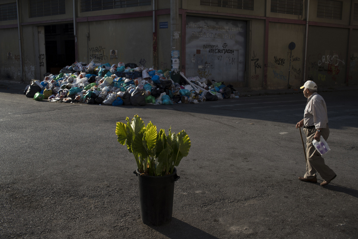 A man looks on a pile of trash as he walks behind a flower pot in Kaminia neighborhood of Piraeus, near Athens, June 27, 2017. Striking garbage collectors who fear job losses from EU-imposed regulations governing short-term contract workers in the public sector, were on the 11th-day of protest that left huge piles of trash around Athens. (AP/Petros Giannakouris)