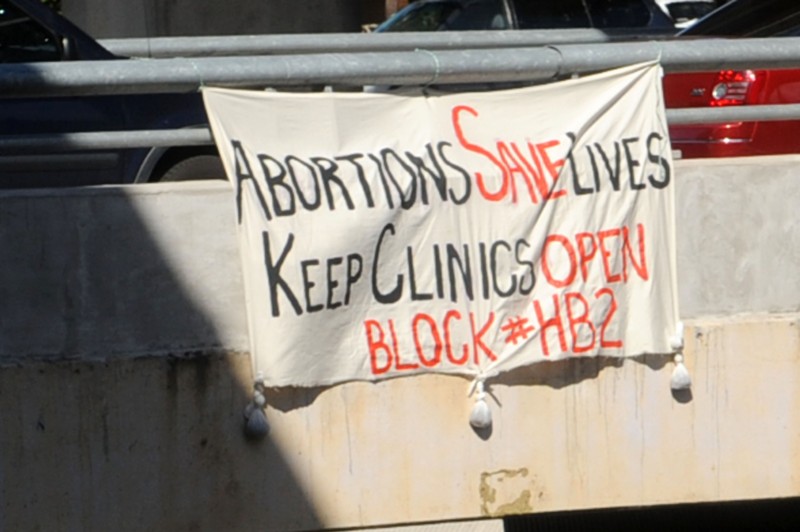 A banner tied to a highway overpass reads: Abortions Save Lives, Keep Clinics Open!