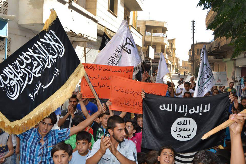 In this photo provided by an anti-Bashar Assad activist group Edlib News Network (ENN) anti-Syrian government protesters carry flags of the al-Qaida-affiliated Nusra Front, left, and Islamic State group, right, during a demonstration against the U.S.-led coalition airtstrikes, at Maarat Masrin town, in Idlib province, northern Syria.