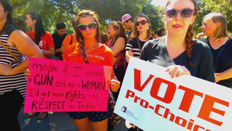 Two activists with signs in a crowd reading: If I were a Gun and not a Woman I'd Get More Rights and Respect In Texas. And: Vote Pro-Choice.