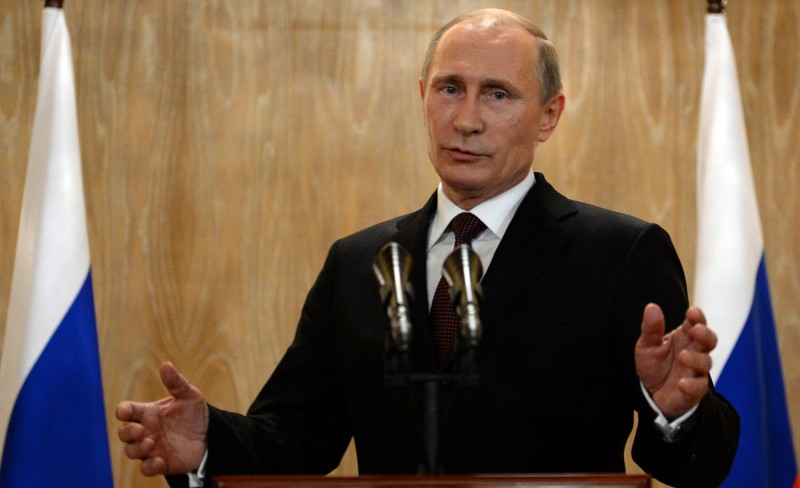 Putin speaks at a podium with his arms outstretched.