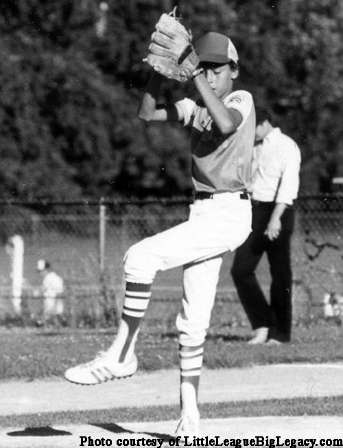 A B&W archive photo of a young Derek Jeter, in a Little League Uniform, practicing his pitching on a baseball diamond.