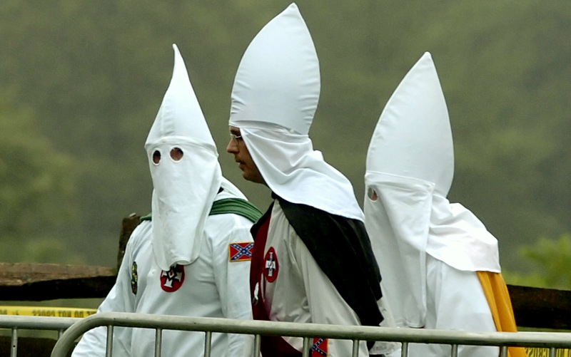 Three members of Klan, two are in hooded robes while one has his head covered but his face exposed.