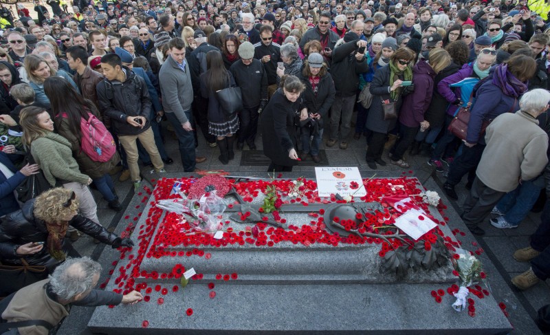 A huge crowd surrounds the tomb which is covered in bright red poppies.