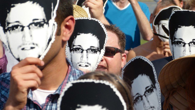A crowd of protesters covers their face with Snowden masks.