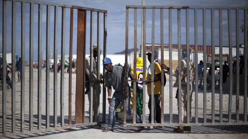 Workers open a massive locked gate as one man crosses the border.