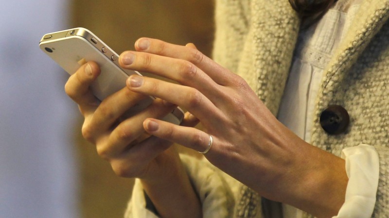 A closeup of a pair of feminine hands and a torso in a sweater The hands are using a smartphone. A ring is on one pinkie.