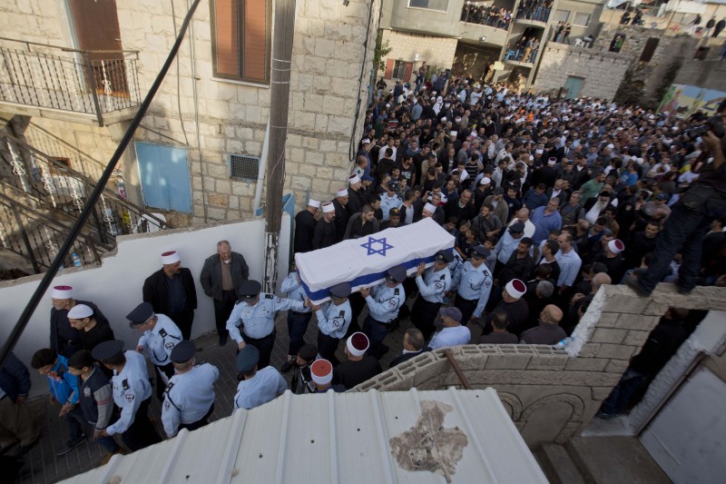 A huge crowd follows a coffin draped in the Israeli flag as it is carried through narrow stone streets in Israel.