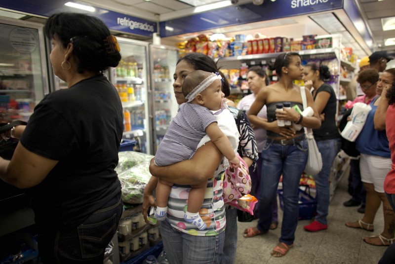 A woman in a market holds a young gir, part of a long line of people waiting in line.