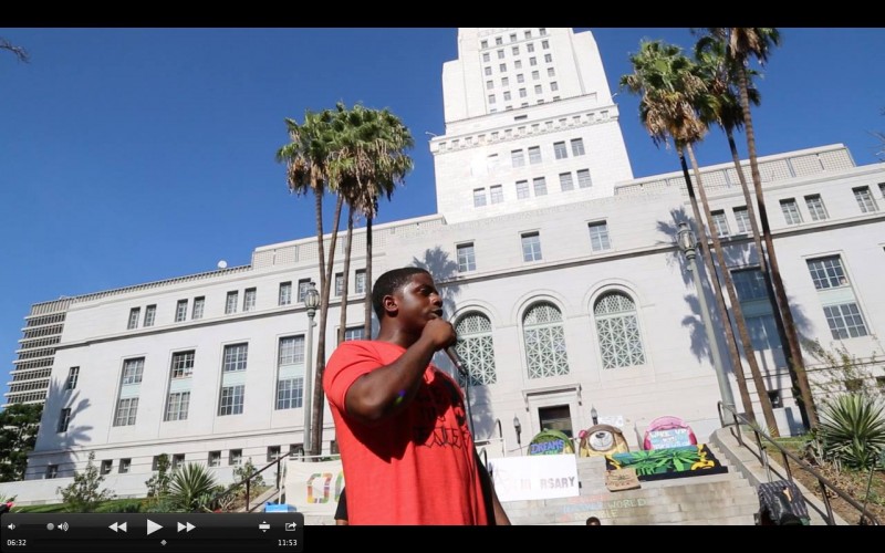 Holding a microphone, Ceebo raps in front of City Hall and Occupy tents.