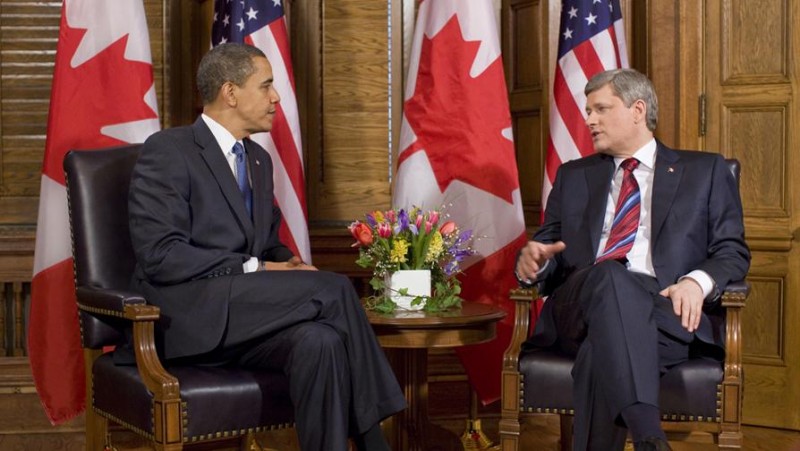 Obama and Harper converse in chairs with the flags of their countries behind them, in a formal photo opportunity.