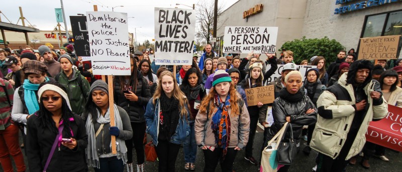 A diverse crowd of protesters in winter clothes. Signs: A Person Is A Person, Black Lives Matter.
