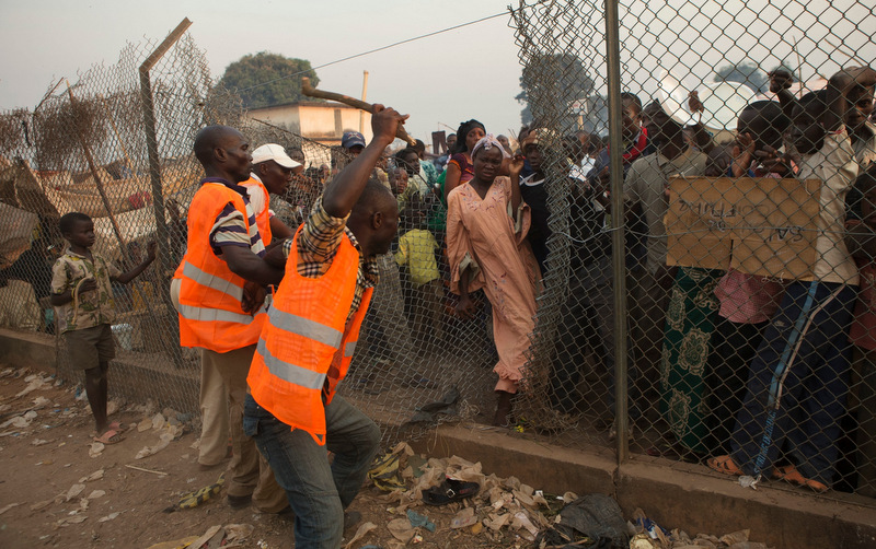 A security volunteer threatens with a stick as people who had been sleeping in a food distribution area try to force their way back in, after being ordered to move to a new settlement area, in an informal camp housing an estimated 100,000 displaced people, at Mpoko Airport in Bangui, Central African Republic, Wednesday, Jan. 8, 2014. Food and supplies distribution by the World Food Program and the United Nations Refugee Agency began Tuesday and was expected to last 10 days. It is the first aid delivery to reach the camp since Dec. 15, and many families were lacking food or even rudimentary shelter from the harsh daytime sun and chilly nights. Residents were receiving supplies including rice, cooking oil, tarps, mats, and blankets. (AP Photo/Rebecca Blackwell)