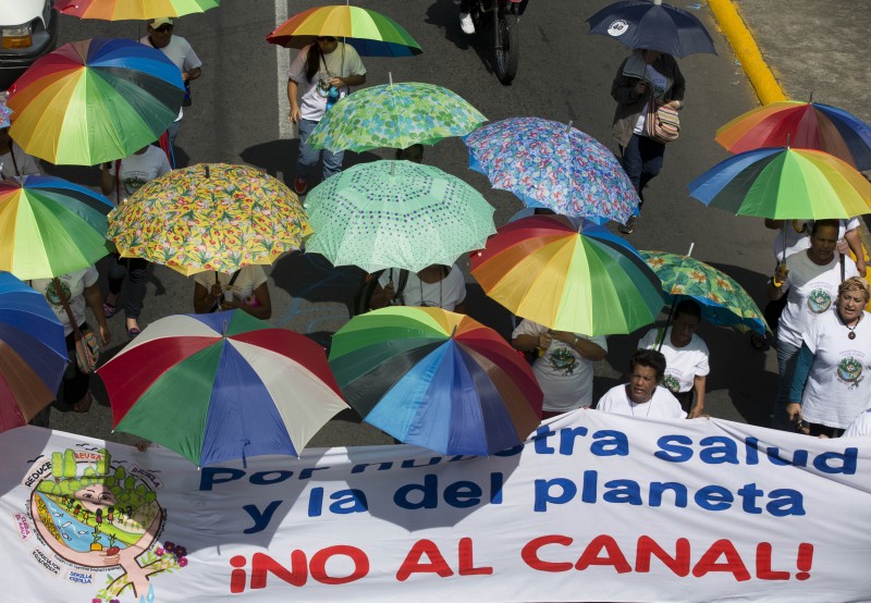 People carry colorful umbrellas and a large banner saying No to the canal.