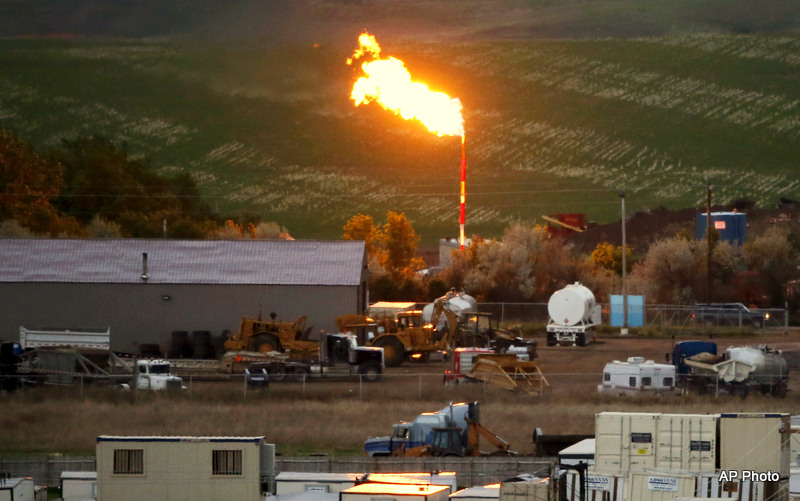 In a large industrial work yard, a smoke stack belches flame from natural gas burn off.