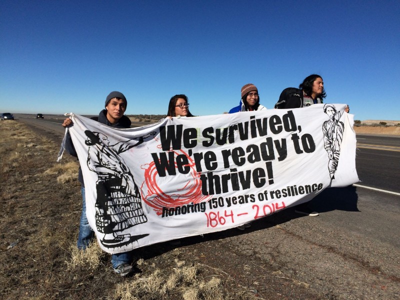 Diné youth activists on traverse Highway 550 in New Mexico earlier this month, part of 200-mile walk across their traditional lands to raise awareness about fracking and other harmful exploitation of the earth. Their banner reads, "We survived, we're ready to thrive. Honoring 150 Years of Resilience, 1864 - 2014." (Facebook / Nihígaal bee Iiná)
