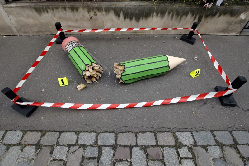 An anonymous art installation showing a broken pencil is displayed on the pavement near the Charlie Hebdo office in Paris, Tuesday, Jan. 20, 2015.  The installation is a large green pencil broken in half, the two halves labelled 1 and 2 with small cards, with red and white tape surrounding the sculpture to form a square museum-style barrier. Terror attacks by French Islamic extremists should force the country to look inward at its "ethnic apartheid," the prime minister said Tuesday as four men faced preliminary charges on suspicion of links to one of the gunmen. (AP Photo/Francois Mori)