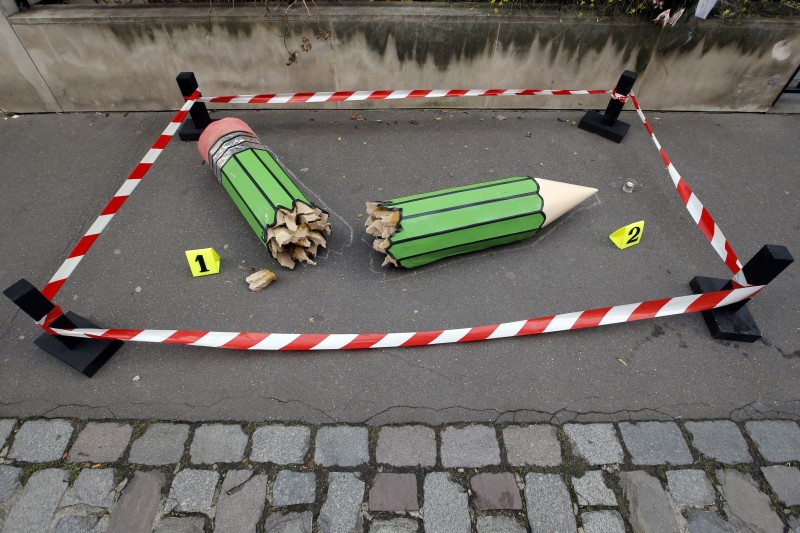 An anonymous art installation showing a broken pencil is displayed on the pavement near the Charlie Hebdo office in Paris, Tuesday, Jan. 20, 2015. The installation is a large green pencil broken in half, the two halves labelled 1 and 2 with small cards, with red and white tape surrounding the sculpture to form a square museum-style barrier. Terror attacks by French Islamic extremists should force the country to look inward at its "ethnic apartheid," the prime minister said Tuesday as four men faced preliminary charges on suspicion of links to one of the gunmen. (AP Photo/Francois Mori)