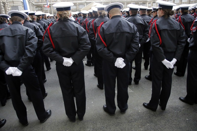 Many rows of officers in formal dress uniform, heads bowed with gloved hands clasped behind their backs.