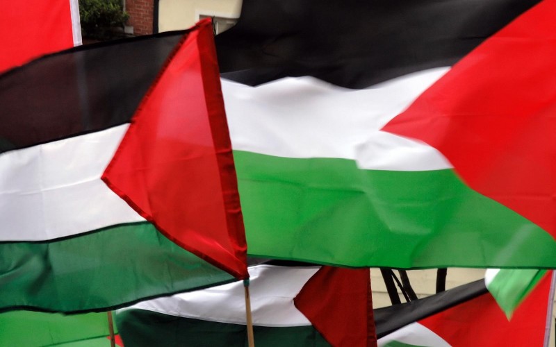 Several Palestinian flags flap in the wind at a protest.