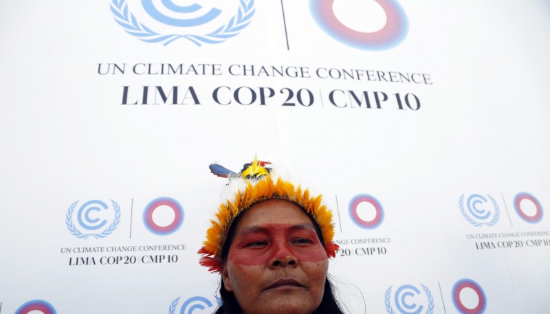 A woman wearing an orange headdress and red facepaint frowns into the camera.