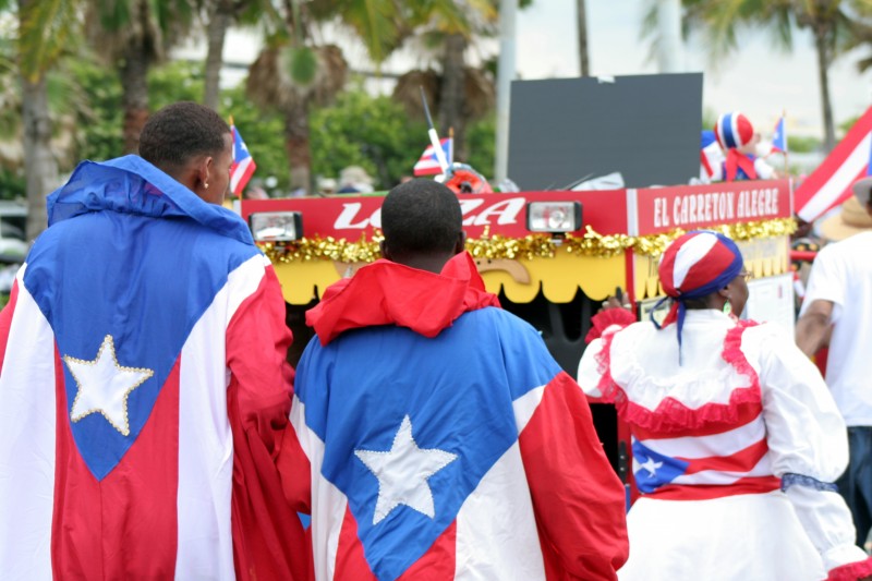 File: Seen from behind, three protesters -- two draped in Puerto Rican flags and a third wearing a flag blouse -- push a float after a protest on May 11, 2006. (Flickr / Oscar Rohena)