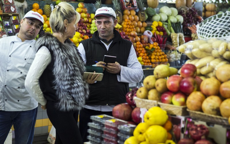 Sellers make a note as a woman selects her purchases from tables covered in colorful fruit, at a food market in central Moscow, Russia, Friday, Jan. 16, 2015. Both the ruble and the MICEX benchmark were down less than 0.5 percent in early trading. Russia's credit rating has been cut by several rating agencies in recent months as the country's economic outlook worsened under the pressure of Western sanctions and declining oil prices. (AP Photo/Pavel Golovkin)