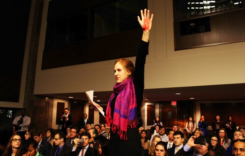 Standing on a chair, an activist holds up her red hand to the camera.