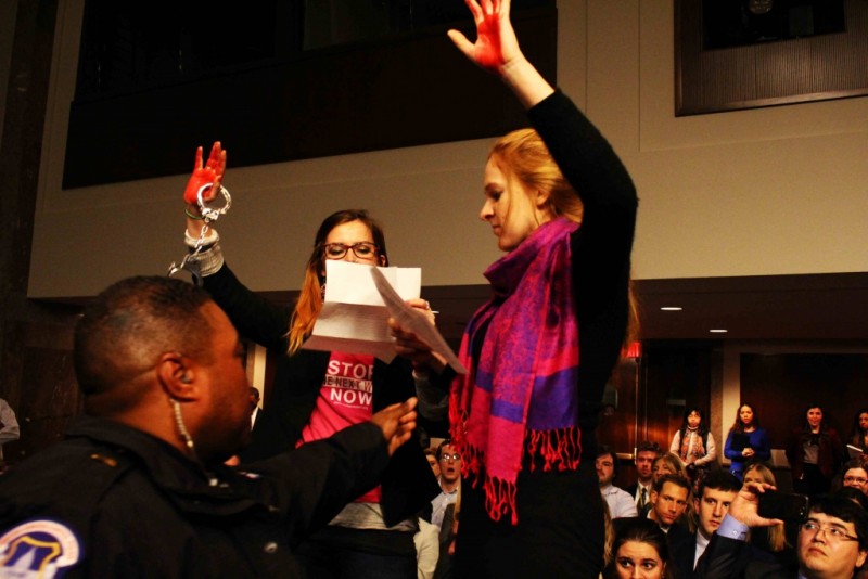 Activists hold up their bloody red hands and a pair of handcuffs as a police officer tries to stop them.