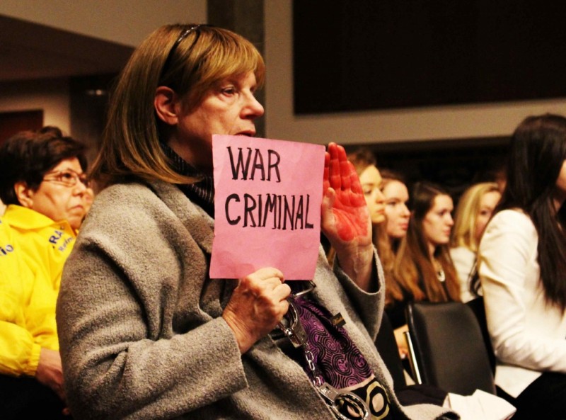 A protester holds up a bloody red hand and a sign reading War Criminal.