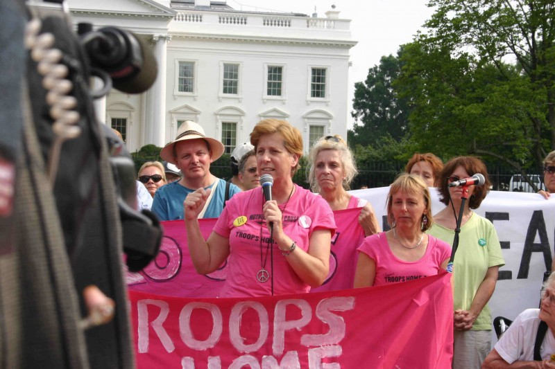 Cindy Sheehan holds a microphone at a White House Rally on July 3, 2006. To her right is Code Pink's Medea Benjamin. A banner, partially visible, appears to read Bring The Troops Home. (Wikimedia Commons / Elvert Barnes)